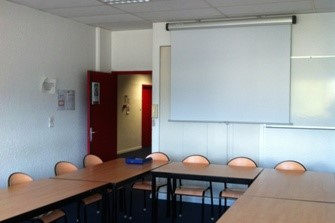 Salle de réunion avec des tables disposés en U et un tableau blanc